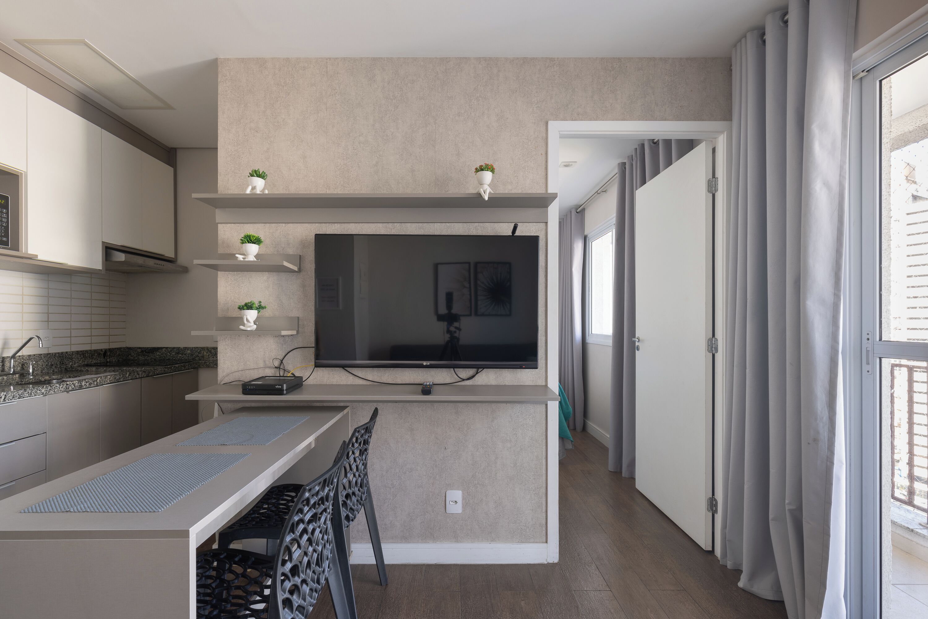 A modern kitchen with a built-in TV, a dining area with a table and chairs, and a window with curtains.