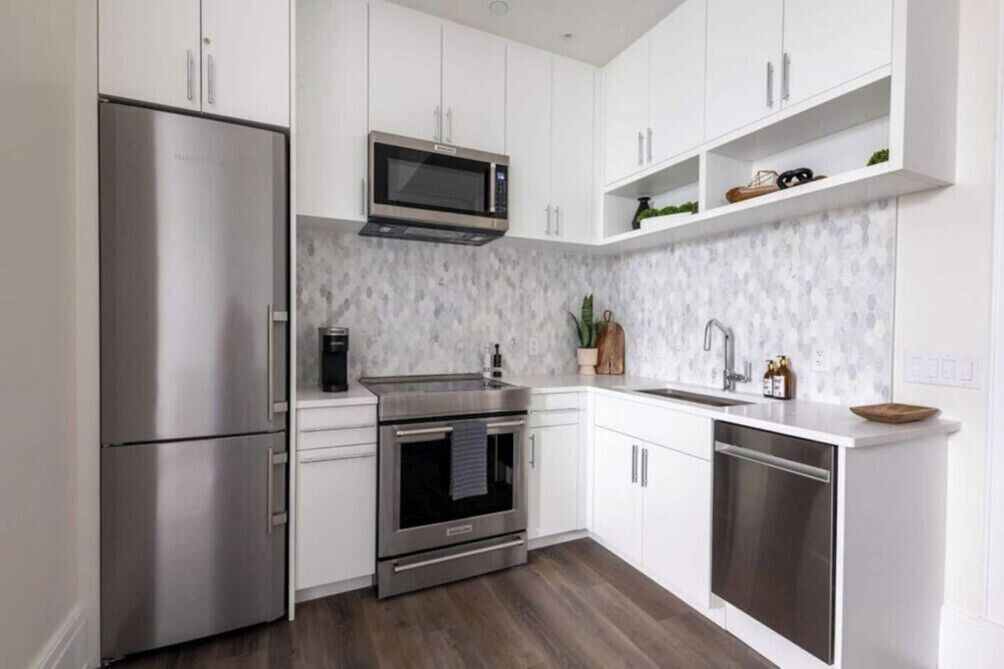 A modern kitchen with stainless steel appliances, white cabinetry, and a marble backsplash.