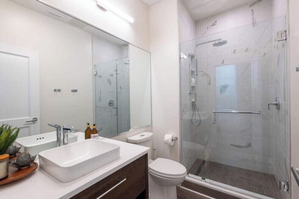 A modern bathroom with a large mirror, a white sink, a toilet, and a glass-enclosed shower area.