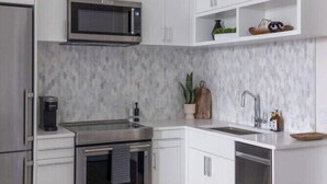 A modern kitchen with white cabinetry, stainless steel appliances, and a marble backsplash. - Chestnut Chateau at the Brent Lofts (Pensacola)