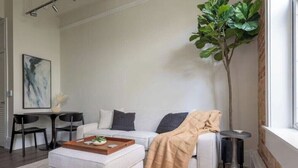 A modern living room with a sofa, ottoman, coffee table, and a potted plant. - Chestnut Chateau at the Brent Lofts (Pensacola)