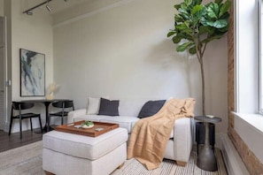 Ein modernes Wohnzimmer mit einer Couch, einem Hocker, einem Couchtisch und einer Topfpflanze.
