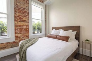 A bedroom with a large bed, a brick wall, and a window. - Chestnut Chateau at the Brent Lofts (Pensacola)