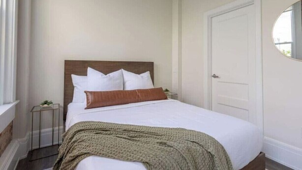 A bedroom with a bed, pillows, a bedside table, and a door. - Chestnut Chateau at the Brent Lofts (Pensacola)