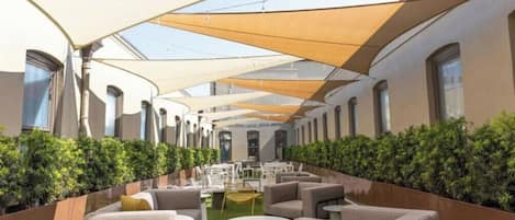 Un espace extérieur aménagé avec des tables et des chaises, entouré de verdure et abrité par une tonnelle.