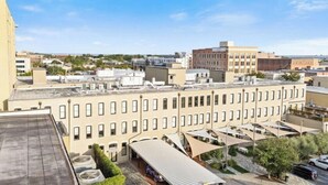 A multi-story building with a flat roof, a covered outdoor seating area, and a parking lot. - Pura Vida at The Brent Lofts (Pensacola)