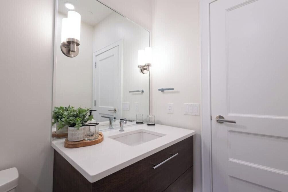 A bathroom with a white sink, dark-toned cabinet, and a door.
