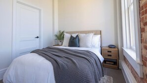 A bedroom with a bed, bedside table, and a window. - Pura Vida at The Brent Lofts (Pensacola)
