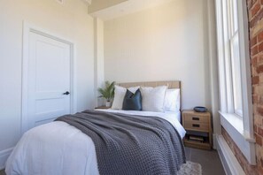 A bedroom with a bed, bedside table, and a window. - Pura Vida at The Brent Lofts (Pensacola)