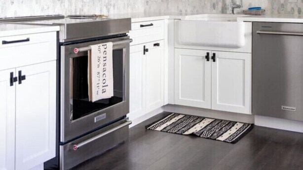 A modern kitchen with white cabinets, a stainless steel oven, a built-in dishwasher, and a backsplash with a speckled pattern. - The Brent Lofts Southern Comfort (Pensacola)