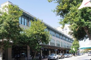 A street view with a building featuring storefronts, parked cars, and trees. - The Brent Lofts Southern Comfort (Pensacola)