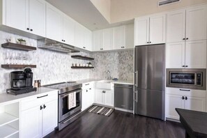 Een moderne keuken met witte kastjes, roestvrijstalen apparatuur en een marmeren spatwand.