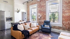 A modern living space with a leather sofa, a blue armchair, and a rustic brick wall. - The Brent Lofts Southern Comfort (Pensacola)