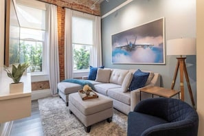 Ein modernes Wohnzimmer mit Sofa, Hocker und Sessel, einem Bild an der Wand und einer Lampe.