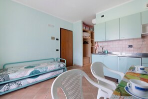 Ein kleines Zimmer mit einem Bett, einem Esstisch mit Stühlen, einer Küchenzeile und einem Kleiderschrank.