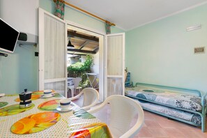 A room with a dining table, chairs, a bed with patterned bedding, a television, and a window with curtains. - Nisportino Vista Mare Apartment with Sea View, Wi-Fi, and Air Conditioning (Rio)