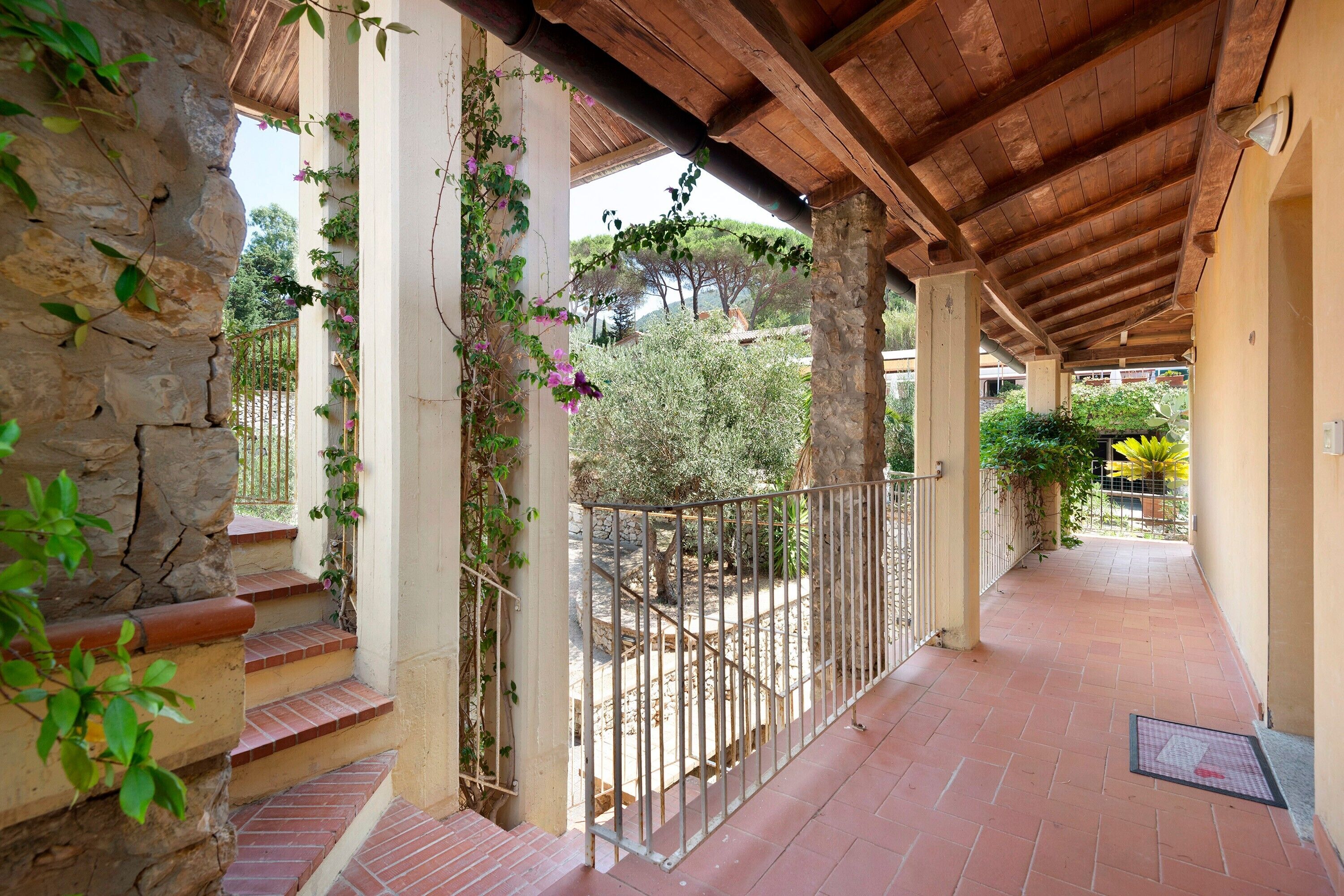 A covered outdoor corridor with stone walls, a metal railing, and a tiled floor.
