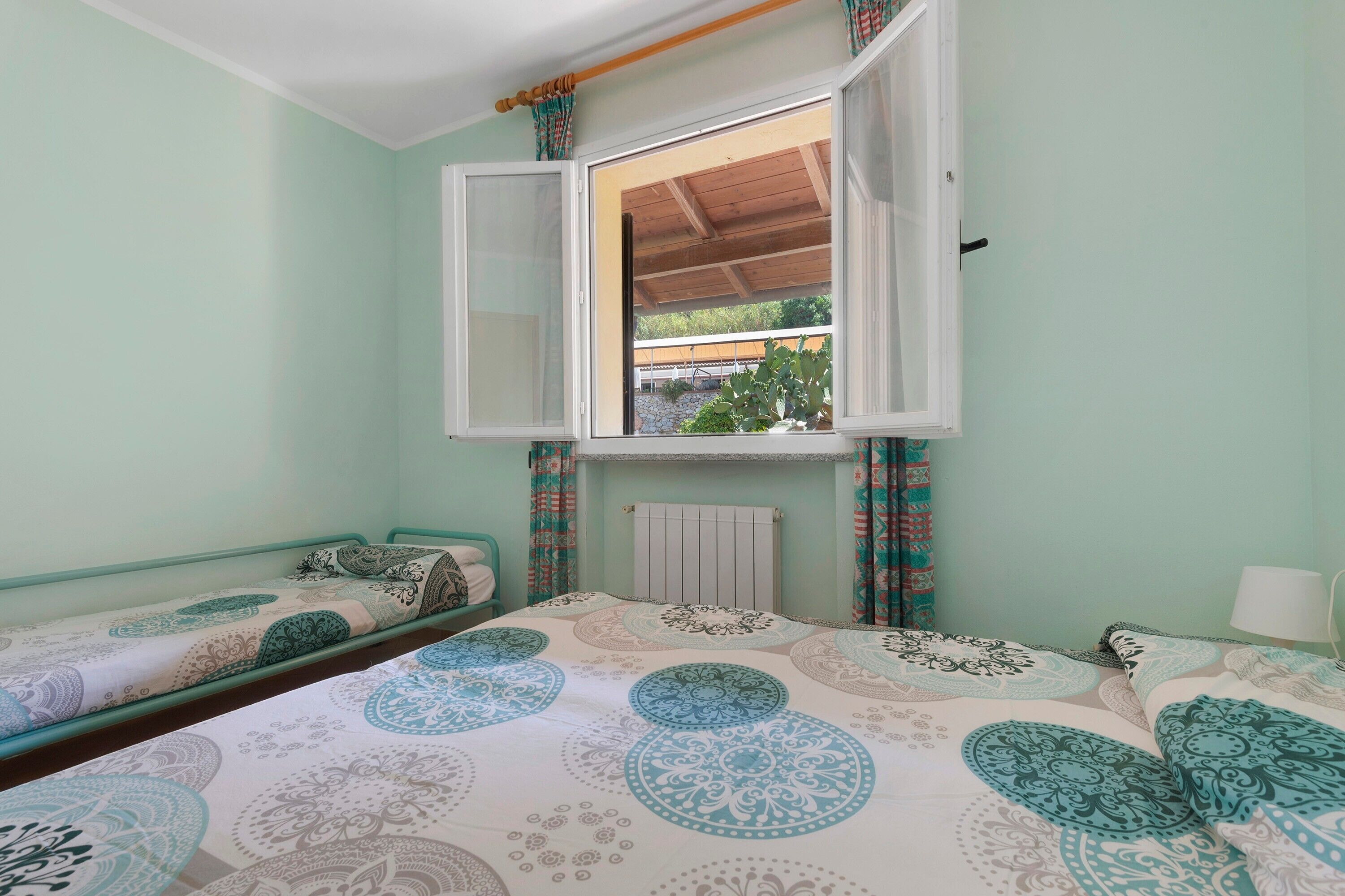 Une chambre avec deux lits simples, une fenêtre avec des rideaux, un radiateur et une vue sur la verdure.