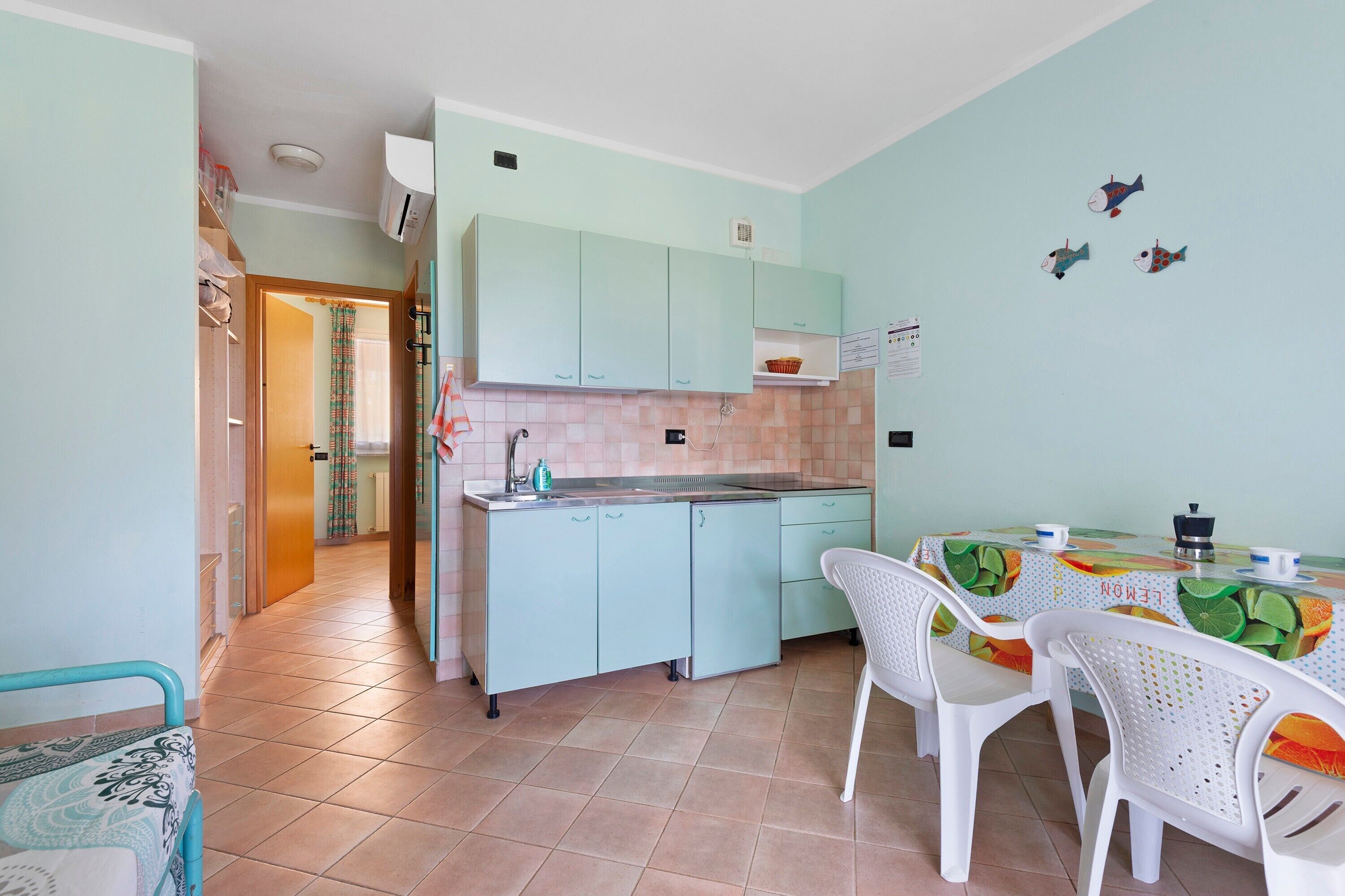 Een compacte keuken met lichtblauwe kastjes, een betegelde spatwand en een eethoek met een tafel en stoelen.