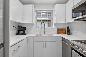 A compact kitchen with white cabinets, a stainless steel sink, a coffee maker, and a stove. - Cozy-Luxe Jr 1BR Apt | Freshly Remodeled & Stylish (Miami Beach)