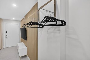 A modern hotel room with a wooden panel wall, a white console table, and a black coat rack with multiple hangers. - Cozy-Luxe Jr 1BR Apt | Freshly Remodeled & Stylish (Miami Beach)