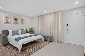 Ein modernes Schlafzimmer mit Bett, Sitzbank, Vorhängen und Wandbildern.