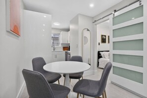 A modern interior with a round dining table, grey chairs, a kitchen area, and a bed with a headboard. - Cozy-Luxe Jr 1BR Apt | Freshly Remodeled & Stylish (Miami Beach)