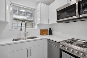 A modern kitchen with a stainless steel sink, a microwave, and a stove. - Cozy-Luxe Jr 1BR Apt | Freshly Remodeled & Stylish (Miami Beach)