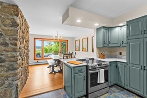 A kitchen with stone walls, a dining area with a view, and a large island with a stove. - CannonView Lodge (Littleton)