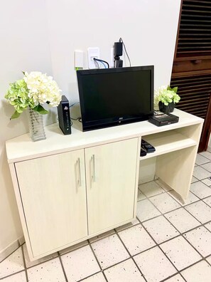 A TV on a white cabinet with two flower vases, a remote, and a power strip. - Apartment 101, beachfront with a balcony overlooking the sea. (Natal)