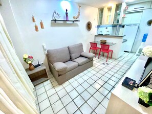 A compact living space with a sofa, a small table, and a kitchenette area. - Apartment 101, beachfront with a balcony overlooking the sea. (Natal)