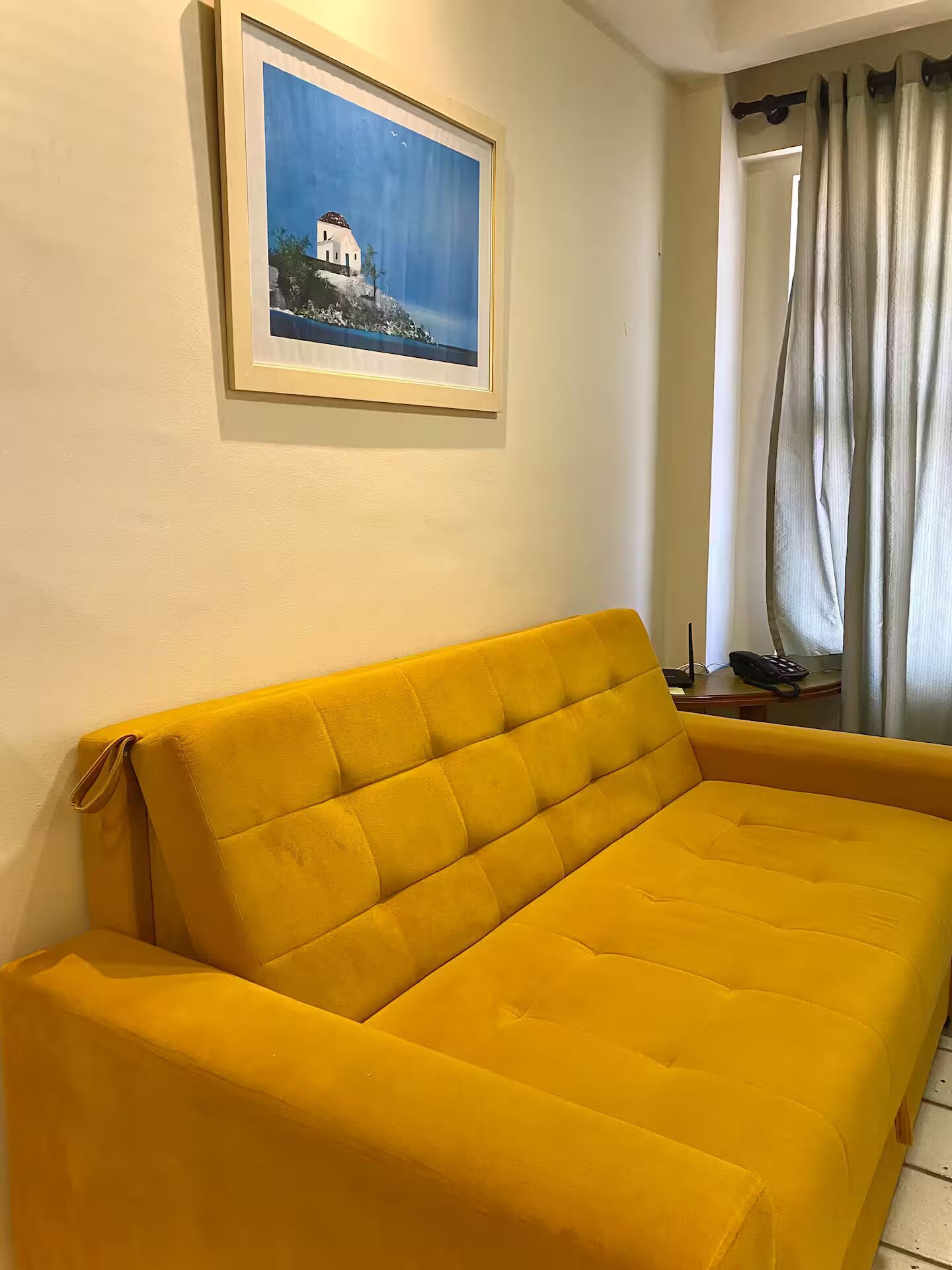 En gul soffa i ett rum med en tavla på väggen som föreställer en vit byggnad.