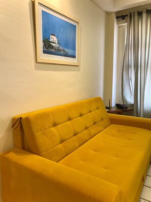 A yellow sofa in a room with a painting of a white building on the wall. - Apartment 108 beachfront (Natal)