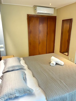 Quarto de hotel com cama, guarda-roupa de madeira, ar condicionado e espelho.