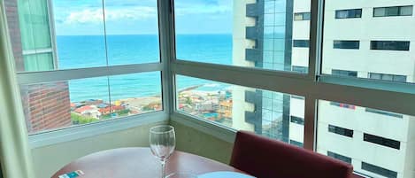 Una mesa de comedor con platos y una copa de vino, frente a una vista del océano y edificios.