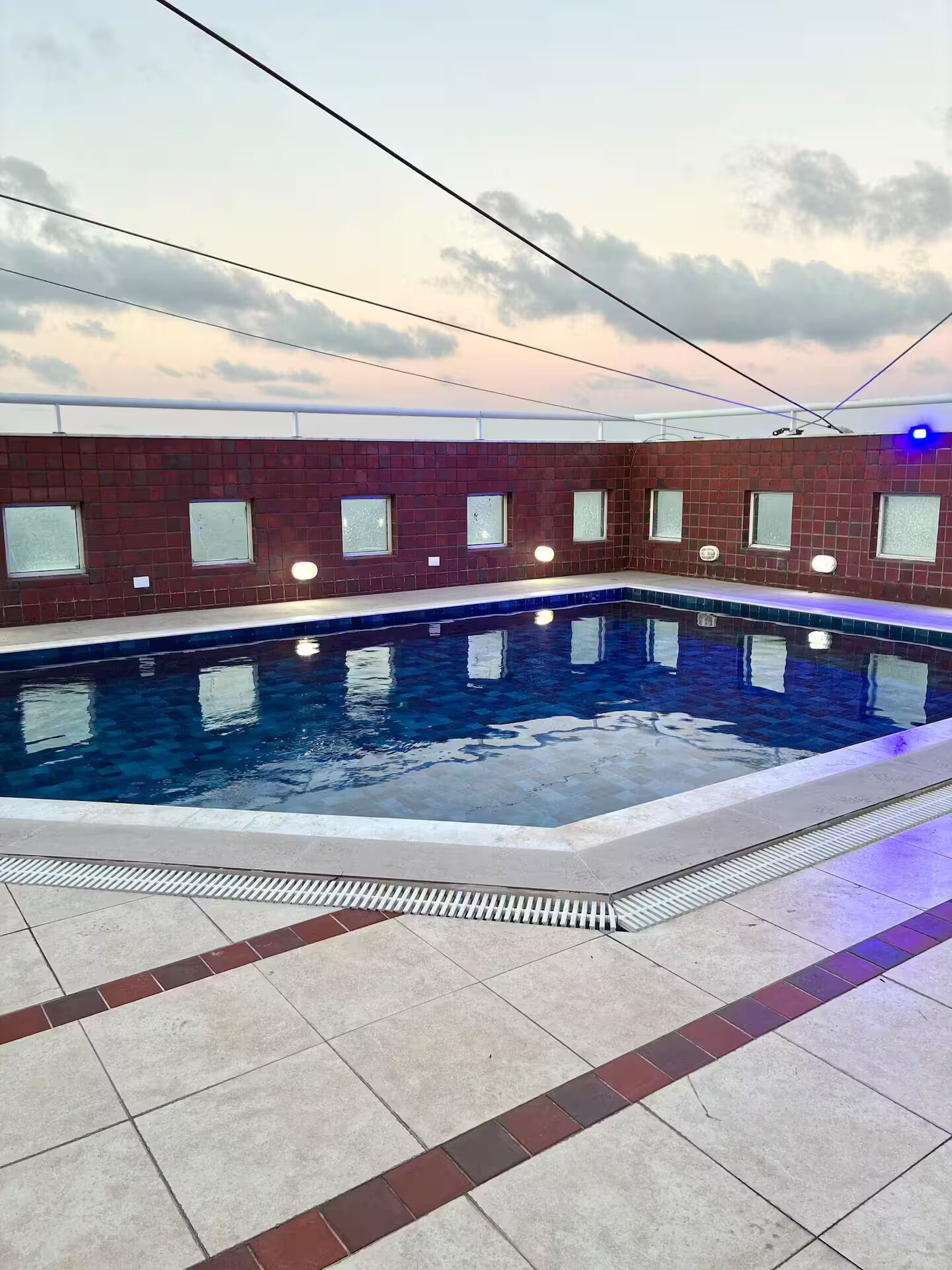 Piscina interior com chão ladrilhado e parede de tijolos.