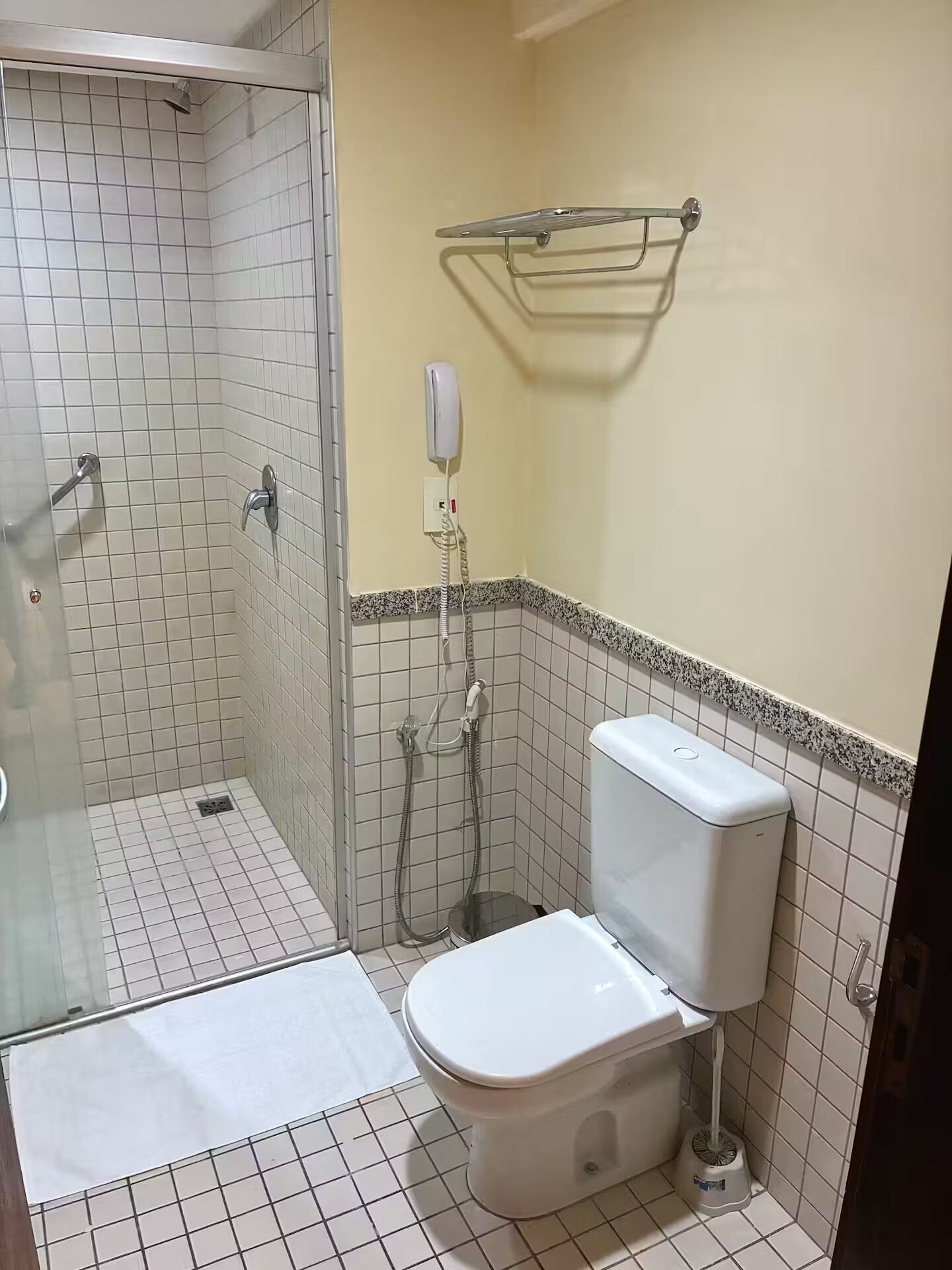 Casa de banho com chuveiro, sanita e secador de mãos fixado na parede.