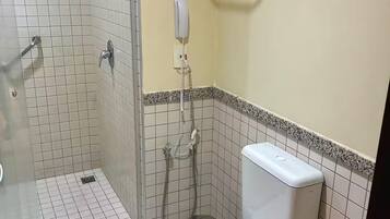 Casa de banho com chuveiro, sanita e secador de mãos fixado na parede.