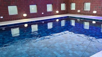 An indoor swimming pool with a tiled floor and walls, surrounded by a brick structure with windows.