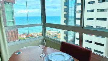 Uma mesa de jantar com pratos e uma taça de vinho, com vista para o oceano e edifícios.