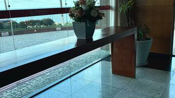 Uma área de recepção com divisória de vidro, balcão de madeira, planta em vaso e vista para o exterior.