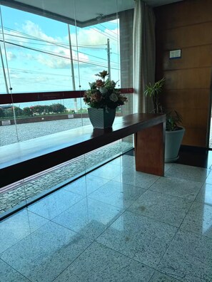 Uma área de recepção com divisória de vidro, balcão de madeira, planta em vaso e vista para o exterior.