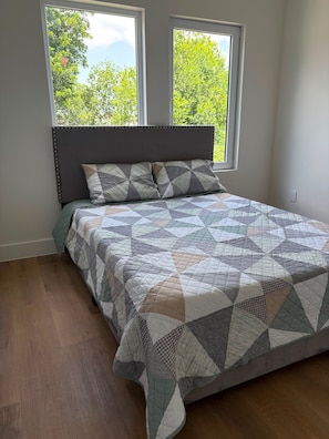 A bedroom with a bed, two windows, and a view of trees.