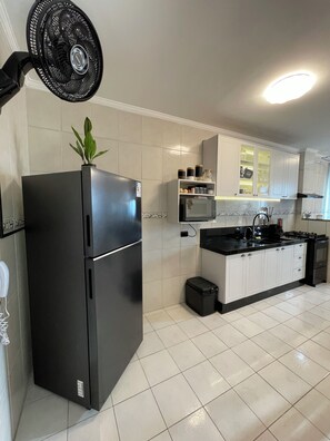 A kitchen with a black refrigerator, a microwave, and a sink. - Modern retreat with barbecue, 200m from the beach. (Praia Grande)