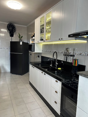 A modern kitchen with white cabinets, a black refrigerator, a black stove, and a black sink. - Modern retreat with barbecue, 200m from the beach. (Praia Grande)