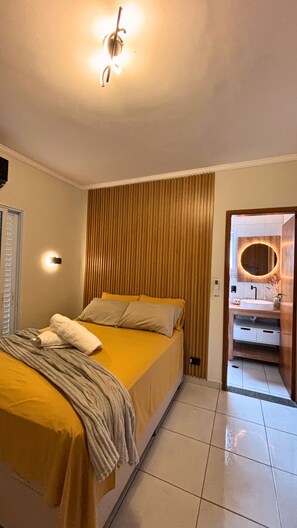 A hotel room with a bed, a bathroom with a round mirror, and a door leading to another room. - Modern Vacation Home with a Grill, 200 meters from the Beach. (Praia Grande)