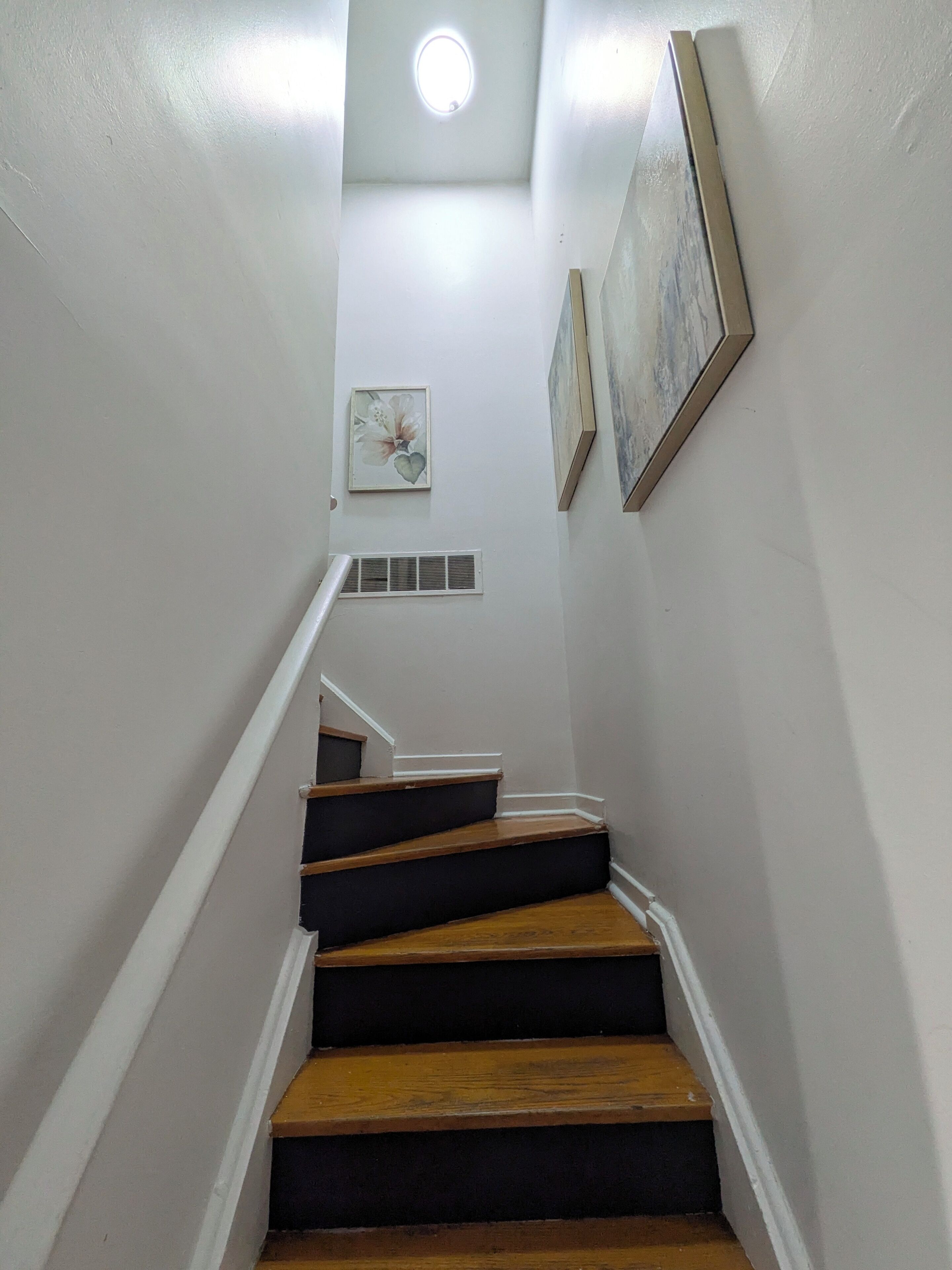 Una escalera de madera con paredes blancas que conduce a una plataforma con una lámpara en el techo.