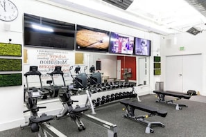 Ein Fitnessraum mit Trainingsgeräten, einer Uhr und einer Wand mit motivierenden Postern.