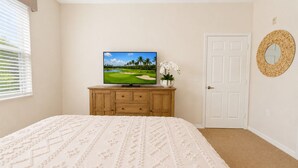 A bedroom with a bed, a television on a wooden dresser, a door, and a wall-mounted mirror. - The Fairway Retreat at GreenLinks (Naples)