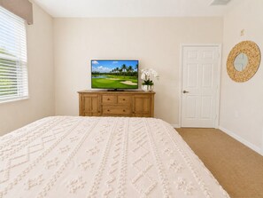 Ein Schlafzimmer mit einem Bett, einem Fernseher auf einer Holzkommode, einer Tür und einem an der Wand befestigten Spiegel.
